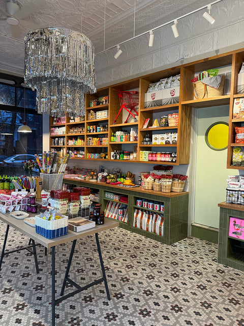 Interior Ándale Market in Lincoln Park, a specialty snack shop with wood shelves, colorful packaged foods, display tables, patterned tile flooring, and a large silver-tinsel chandelier.