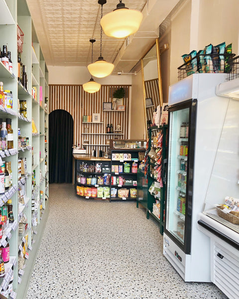 Interior of Ándale Market in Andersonville, a specialty grocery shop with stocked shelves, a central checkout counter, pendant lights, and refrigerated displays.