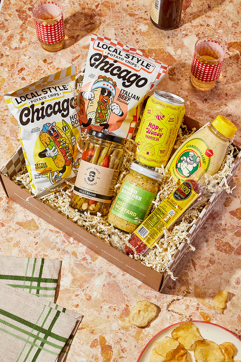 Gourmet gift box with Chicago-themed snacks and drinks on a marble surface.