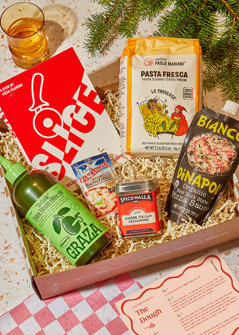 Pantry gift set with pizza ingredients and a glass of beer on a checkered tablecloth.