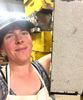 Bike A Bee founder in a baseball cap and apron posing beside a honeycomb panel.