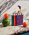 Three colorful patterned cutting boards on a marble surface with fruit props and a flower stem around them.