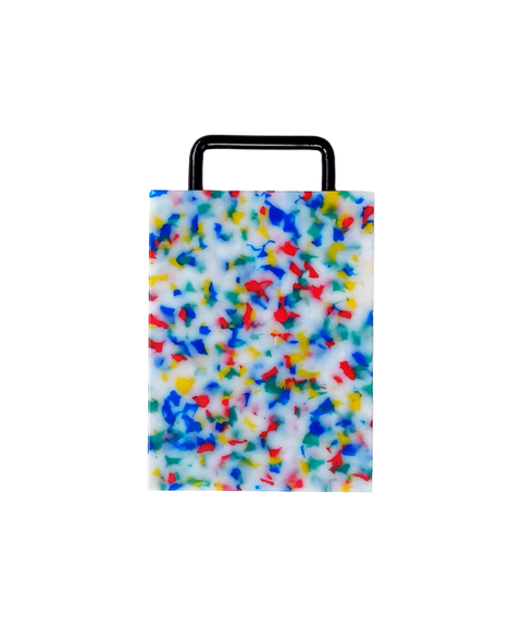 A rectangular plastic cutting board with a black metal handle, featuring a white base covered in dense multicolored confetti-like speckles in blue, red, yellow, and green, shown on a plain white background.