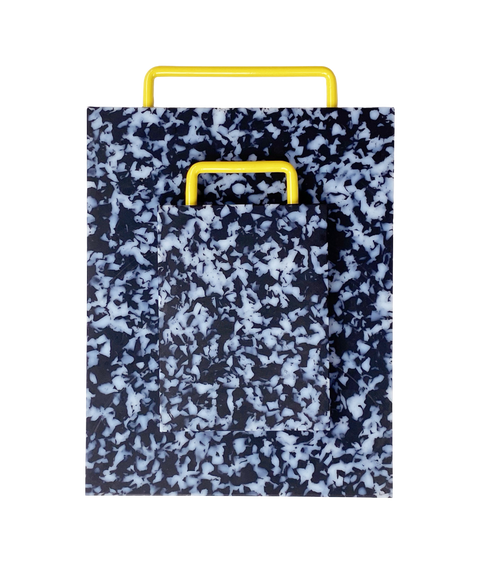 A rectangular plastic cutting board with a black and white marbled pattern and yellow metal handle, shown on a plain white background. There is a smaller matching version of the same cutting board on top of the larger one.