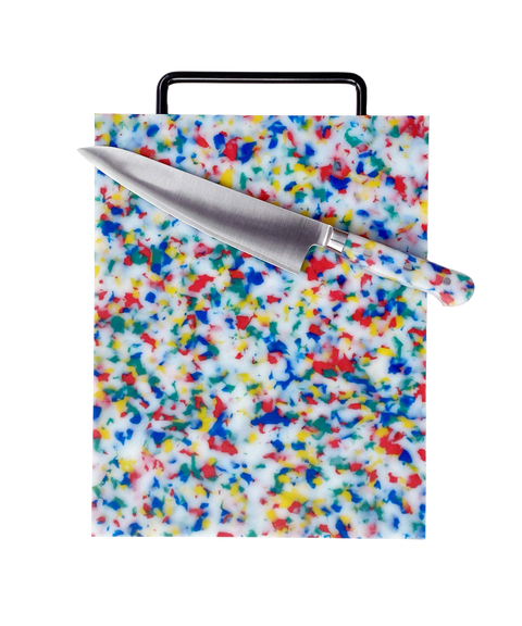 A rectangular cutting board with a multicolor speckled pattern on a white base, featuring a black handle and shown with a stainless steel chef's knife on top, isolated on a white background.