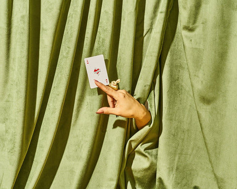 Hand holding a gift card that looks like a playing card behind a green curtain