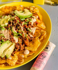 Loaded nachos in a large yellow bowl with a roll of Hellenic Farm Fig Salami in the foreground.