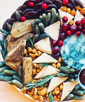 An overhead close-up of a cheese board  featuring sliced cheeses, nuts, fruit and Hellenic Farms Fig Salami.