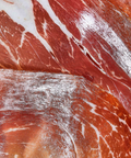 Close-up of cured meat slices with visible fat marbling, showing red and pink tones with white fat streaks.