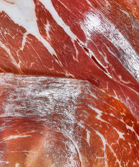 Close-up of cured meat slices with visible fat marbling, showing red and pink tones with white fat streaks.