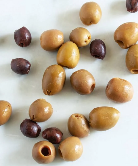 A scattered arrangement of whole olives in green and dark purple tones on a plain white surface.