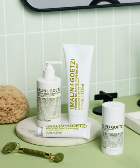 A set of Malin + Goetz skincare products arranged on a light green countertop with a tiled backsplash.