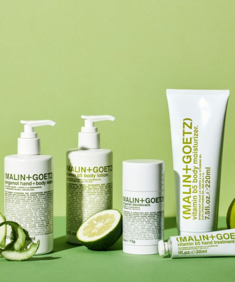 A set of Malin + Goetz skincare products arranged on a light green surface against a matching green background. 
