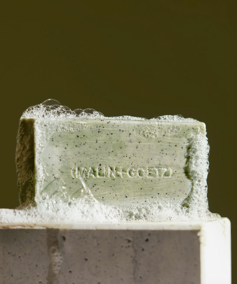 A pale green Malin + Goetz soap bar covered in bubbles.