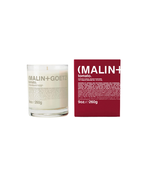 A Malin+Goetz Tomato candle in a clear glass jar next to its dark red box.