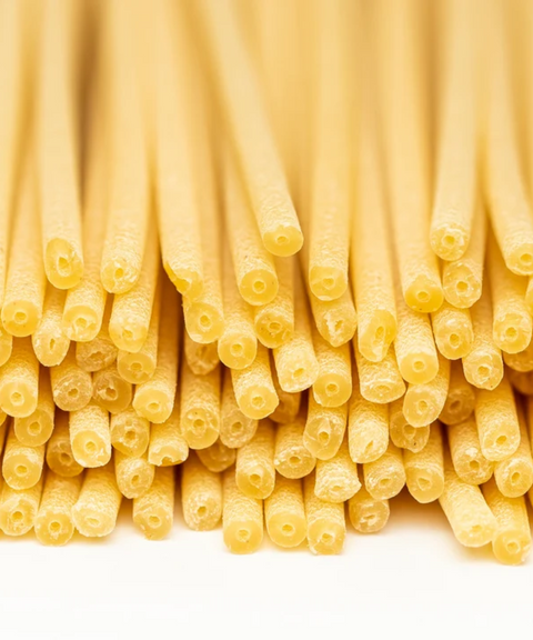 Close-up of uncooked bucatini pasta on a white background.