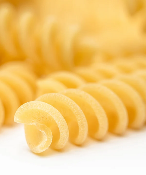 Close-up of uncooked fusilli pasta on a white background.