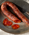 A close-up of U-shaped Palacios chorizo on a metal plate, with several thick slices  and a knife.