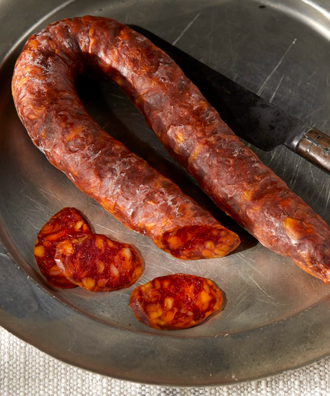 A close-up of U-shaped Palacios chorizo on a metal plate, with several thick slices  and a knife.