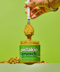 Hand holding a spoonful of chunky pistachio butter over an open jar of Pistakio Crunch.