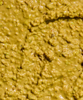 Close-up of a glossy, chunky yellow-green pistachio spread with brown and green flecks.
