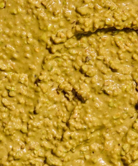 Close-up of a glossy, chunky yellow-green pistachio spread with brown and green flecks.