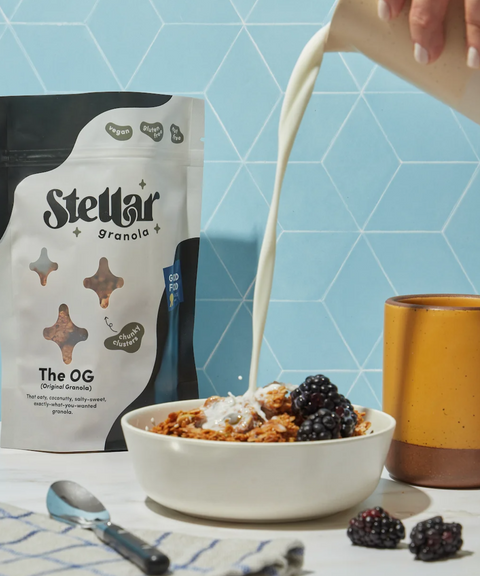 A bag of Stellar Granola 'The OG' next to a bowl of granola being poured with milk and berries.