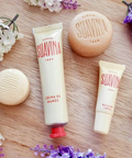 Three Suavina skincare products arranged on a light wood surface with small white and purple flowers.