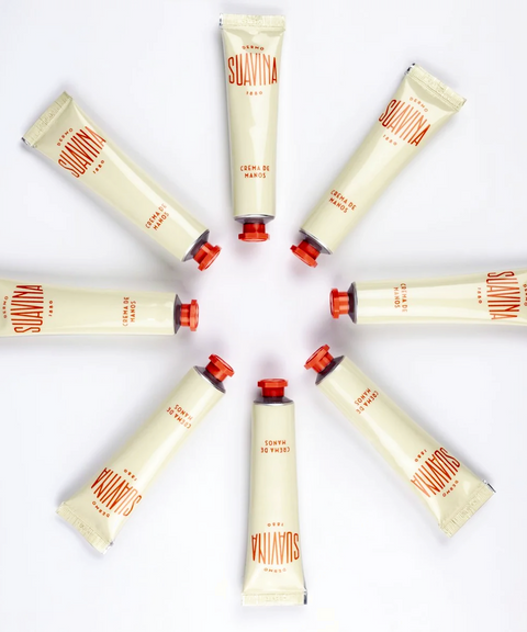 Six tubes of Suavina hand cream arranged in a circular pattern. The tubes are a cream color with coral branding and caps.