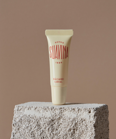 A cream-colored Suavina original lip balm tube stands upright on a textured stone block against a solid taupe background.