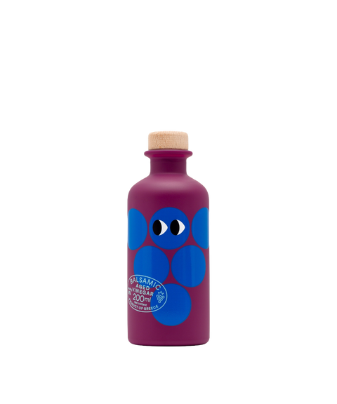 A purple bottle of Yiayia and Friends Aged Balsamic Vinegar with blue circles, cartoon eyes and a wooden cap.