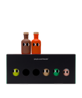 Two small bottles of olive oil with cartoon eyes, one brown and one orange, displayed on top of a black box labeled 'Yiayia and Friends' against a white background.