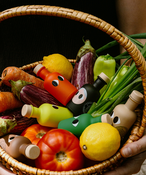 A wicker basket filled with colorful vegetables and small bottles of Yiayia & Friends olive oil.