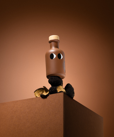 A brown bottle of Yiayia & Friends truffle olive oil with a wood stopper balanced on black truffles on a pedestal.