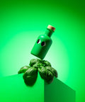 A green bottle of Yiayia & Friends basil olive oil with a wood stopper balanced on basil leaves on a pedestal.