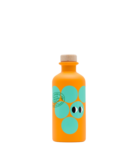 An orange bottle of Yiayia and Friends White Balsamic Vinegar with aqua circles, cartoon eyes and a wooden cap.