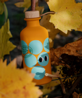 An orange bottle of Yiayia and Friends White Balsamic Vinegar with aqua circles, cartoon eyes and a wooden cap, set amongst fall leaves.